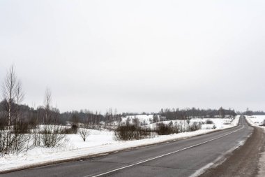 Kış sezonu kırsal asfalt yol. Kirli yol çatlaklar. Kış alanları ve orman bulutlu bir günde