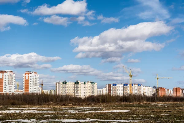 View of the field with a frozen pond and the outskirts of the city, new city under construction, spring sunny day — Stock Photo, Image