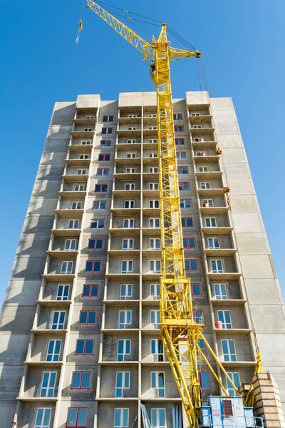 yellow tower crane and the construction of a multi-storey building against a blue sky
