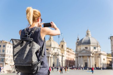 Kadın turist bir fashinable vintage hipster sırt çantası alarak fotoğraf ile Piazza del Popolo Roma, İtalya tarafından cep telefonu.