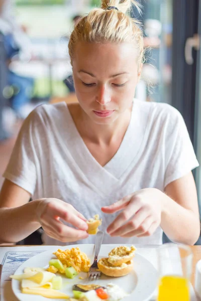 Mujer comiendo delicioso desayuno saludable: huevos revueltos, queso, verduras, pan y jugo de naranja . — Foto de Stock