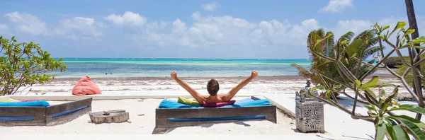 Relaxed man in luxury lounger, arms rised, enjoying summer vacations on beautiful beach.