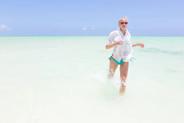 Joven mujer activa divirtiéndose corriendo y salpicando en el agua de mar compañero . — Foto de Stock