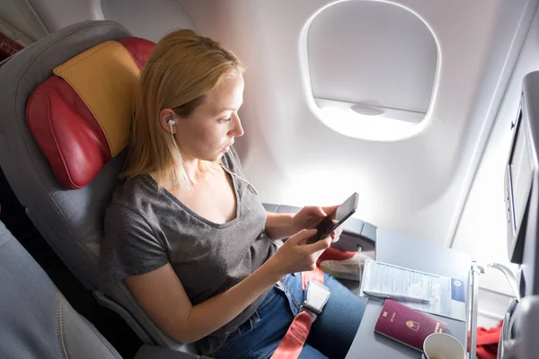 Mulher ouvindo música no telefone inteligente no avião comercial de passageiros durante o voo . — Fotografia de Stock