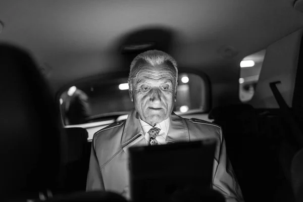 Businessman with a digital tablet sitting in the back seat of a car