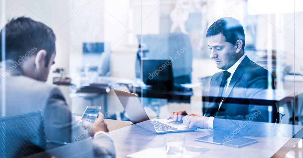 Two young businessmen using laptop computer at business meeting.