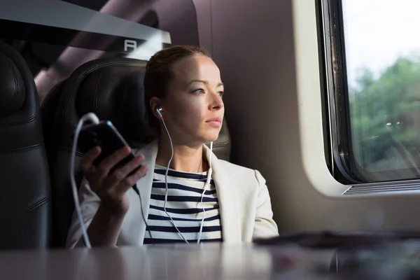 Nachdenkliche Geschäftsfrau hört Podcast auf dem Handy, während sie mit dem Zug reist. — Stockfoto