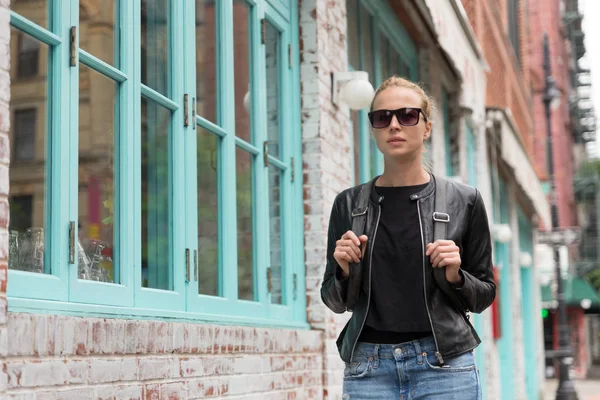 Siyah deri ceket ve meşgul bir şehir sokakta yürürken cep telefonu ile şık genç kadın