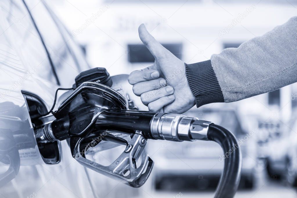 Petrol or gasoline being pumped into a motor vehicle car. Closeup of man, showing thumb up gesture, pumping gasoline fuel in car at gas station.
