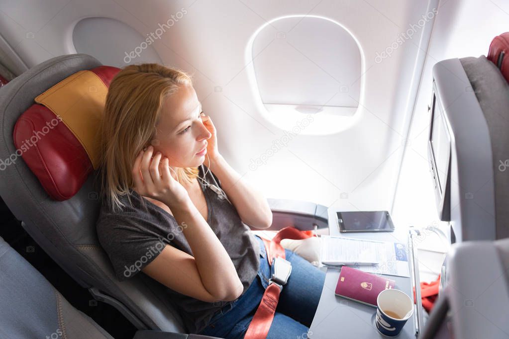 Woman flying on commercial passengers airplane, listening to music.