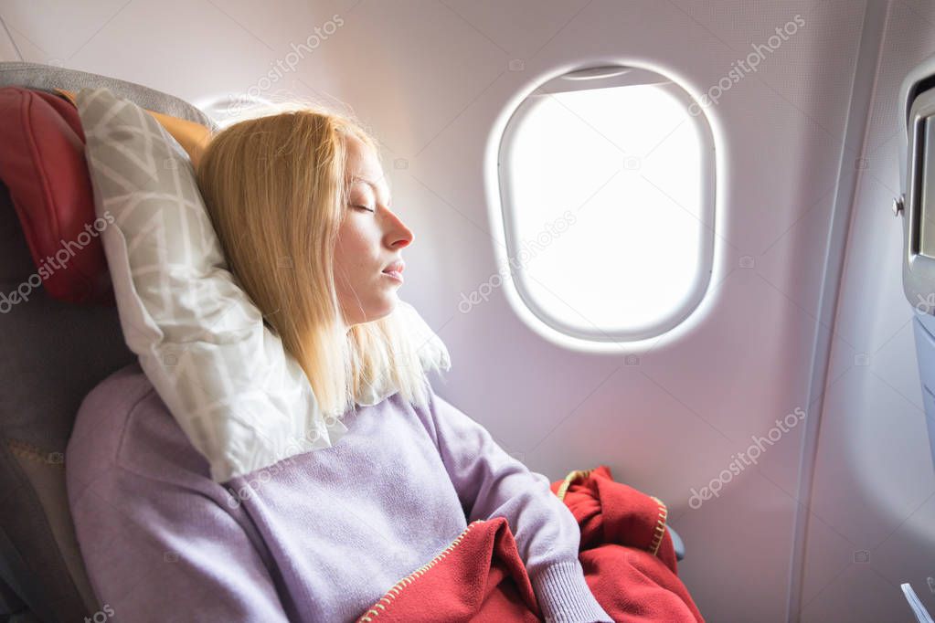 Tired blonde casual caucasian lady sleepin on seat while traveling by airplane. Commercial transportation by planes.