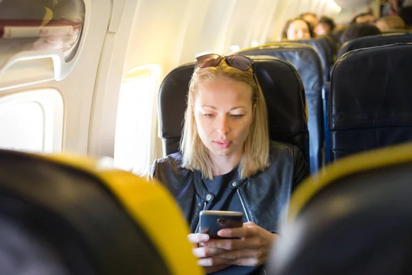 Kvinna med mobiltelefon som underhållning på flygplan under kommersiell flygning. — Stockfoto