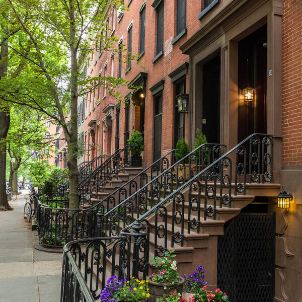 Row of old brownstone buildings along an empty sidewalk block in the Greenwich Village neighborhood of Manhattan, New York City, NYC, USA.