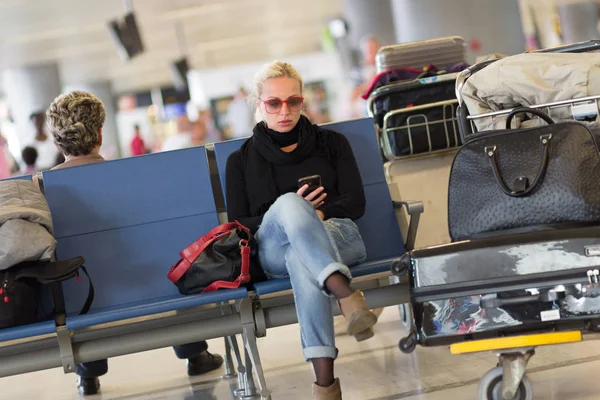 Călător de sex feminin folosind telefonul mobil în timp ce așteaptă . — Fotografie, imagine de stoc