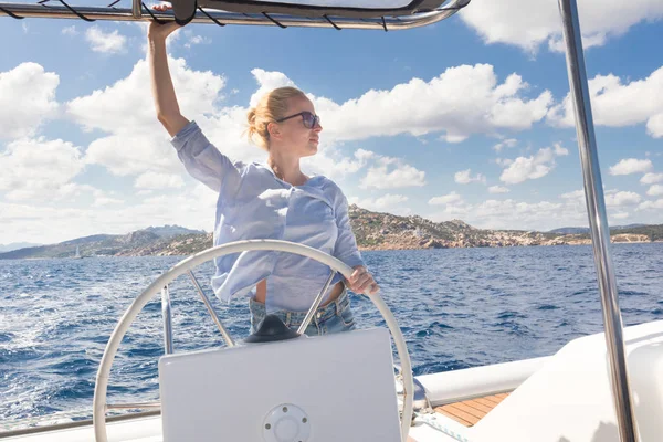Aantrekkelijke blonde vrouwelijke schipper navigeren de fancy catamaran zeilboot op zonnige zomerdag op kalme blauwe zeewater. — Stockfoto