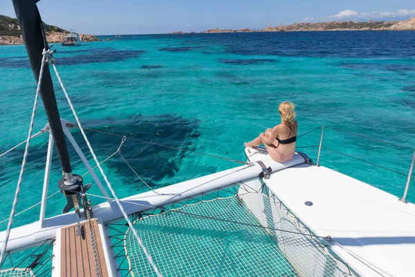 Woman relaxing on a summer sailing cruise, sitting on a luxury catamaran in picture perfect turquoise blue lagoon near Spargi island in Maddalena Archipelago, Sardinia, Italy.