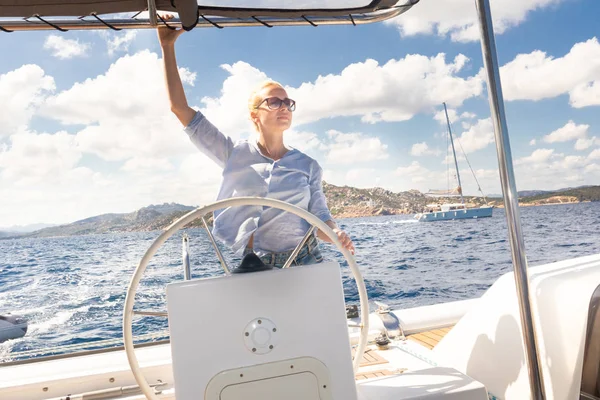 Attraktiva blonda kvinnliga skeppare navigera fancy katamaran segelbåt på solig sommardag på lugna blå havsvatten. — Stockfoto