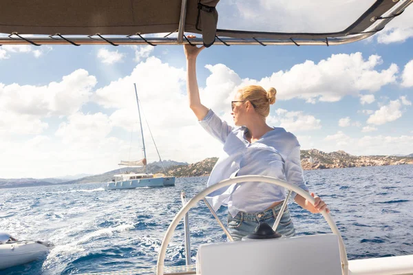 Attraktiva blonda kvinnliga skeppare navigera fancy katamaran segelbåt på solig sommardag på lugna blå havsvatten. — Stockfoto