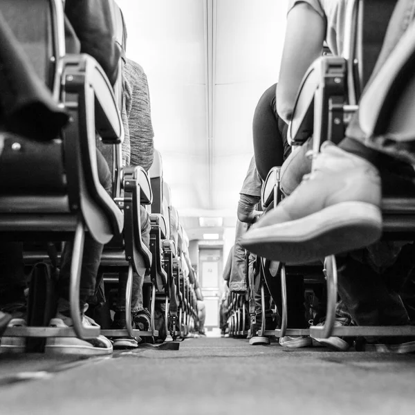 Low agle view of passenegers commercial airplane aisle with passenegers sitting on their seats while flying. Black and white photo. — Stock Photo, Image