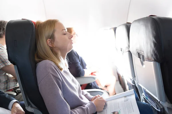 Tired blonde casual caucasian lady napping on seat while traveling by airplane. Commercial transportation by planes. — Stock Photo, Image