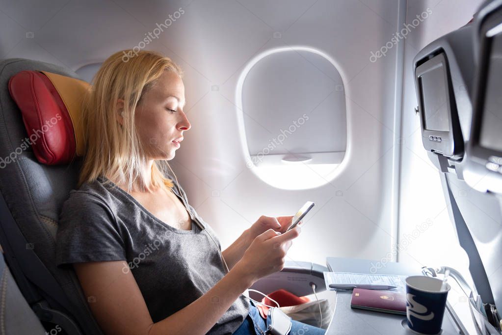 Woman listening to music on smart phone on commercial passengers airplane during flight.