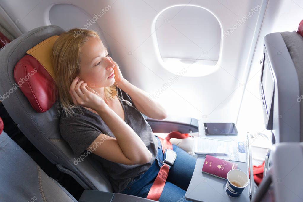 Woman listening to music on smart phone on commercial passengers airplane during flight.