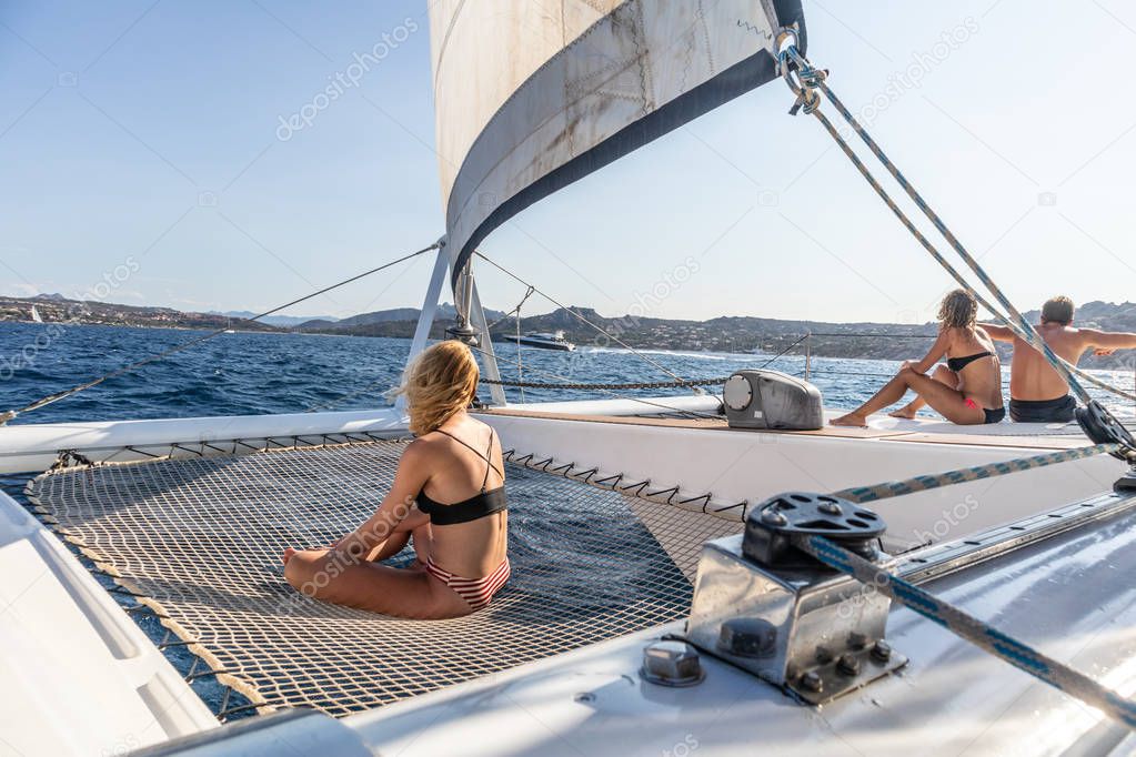People relaxing on a summer sailing cruise, sitting on a luxury catamaran near picture perfect Palau town, Sardinia, Italy.