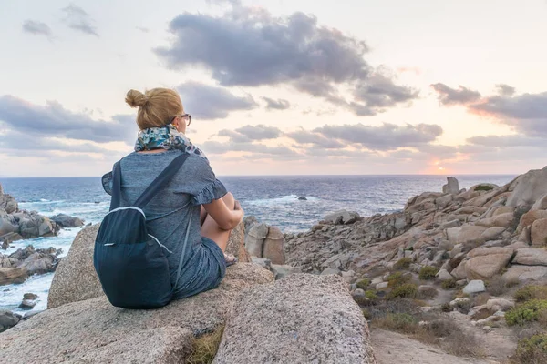 Solo jonge vrouwelijke reiziger horloges een prachtige zonsondergang op spectaculaire rotsen van Capo Testa, Sardinië, Italië. — Stockfoto