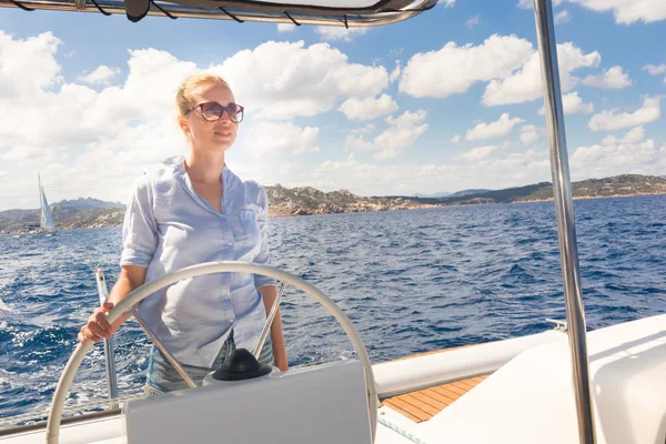 Attraktiva blonda kvinnliga skeppare navigera fancy katamaran segelbåt på solig sommardag på lugna blå havsvatten. — Stockfoto