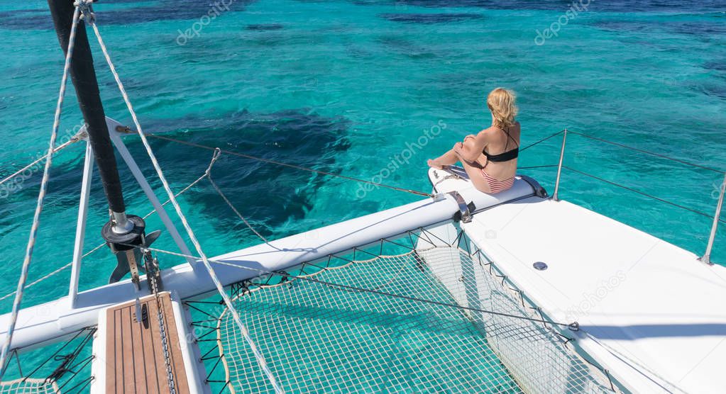Woman relaxing on a summer sailing cruise, sitting on a luxury catamaran in picture perfect turquoise blue lagoon near Spargi island in Maddalena Archipelago, Sardinia, Italy.