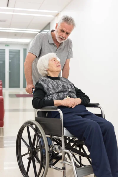 Homem de meia idade ajudando e levando para idosos 95 anos de idade mulher sentada na cadeira de rodas . — Fotografia de Stock