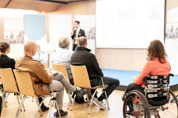 Rear view of nrecognizable woman on a wheelchair participating at business conference talk.