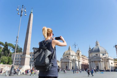 Kadın turist bir fashinable vintage hipster sırt çantası alarak fotoğraf ile Piazza del Popolo Roma, İtalya tarafından cep telefonu.