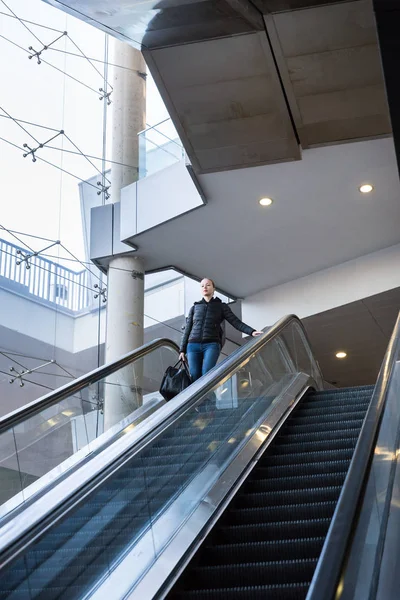 Mujer de negocios con gran bolsa negra y teléfono móvil descendiendo en escaleras mecánicas . —  Fotos de Stock