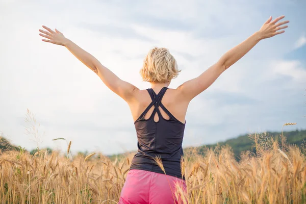 Relaxado mulher desportiva, braços erguidos, apreciando a natureza na bela manhã no campo de trigo . — Fotografia de Stock