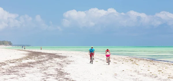 Active sporty tourist couple cycling down picture perfect white sand tropical beach of Paje, Zanzibar, Tanzania. — Stock Photo, Image
