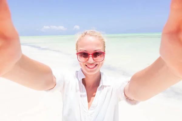 Young woman wearing white beach tunic taking selfie on tropical white sandy beach. — Stock Photo, Image