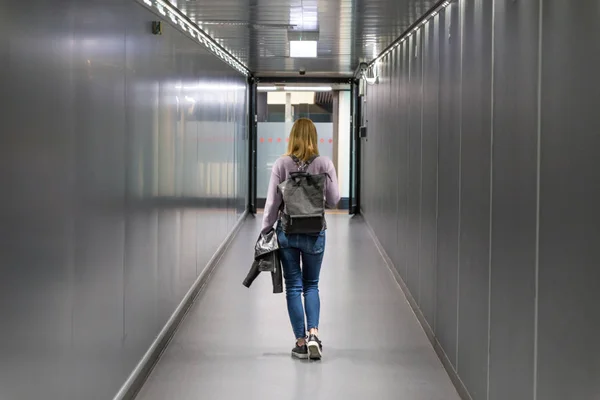 Οπίσθια όψη ενός casual γυναικεία ταξιδιώτη περπάτημα στενό ένα διάδρομο αεροδρομίου. — Φωτογραφία Αρχείου