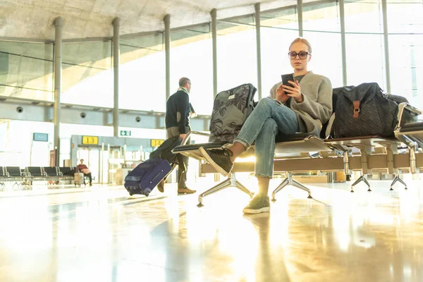 Viajero femenino usando su teléfono celular mientras espera para abordar un avión a las puertas de salida en la terminal del aeropuerto . — Foto de Stock