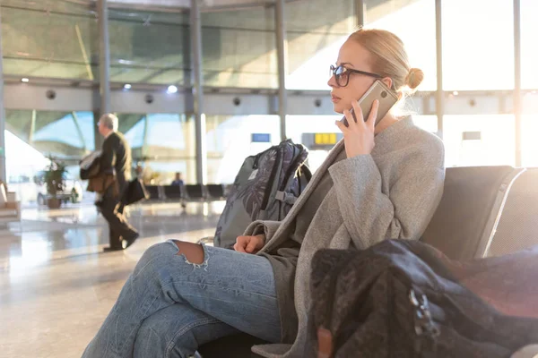 Kvinnliga resenären talar i hennes mobiltelefon medan du väntar på att ombord på ett plan på avgångsportarna på flygplats terminal. — Stockfoto