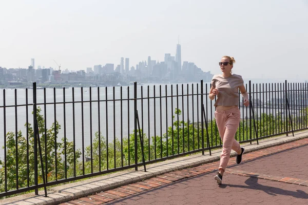 Healthy lifestyle. Woman is jogging on Hamilton ave by Hamilton park, New Jersey. Manhattan of New York City in the background. Stock Picture