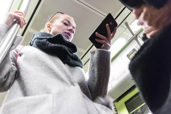 Mulher loira bonita vestindo casaco de inverno e lenço lendo no telefone enquanto viaja de metro transporte público . — Fotografia de Stock