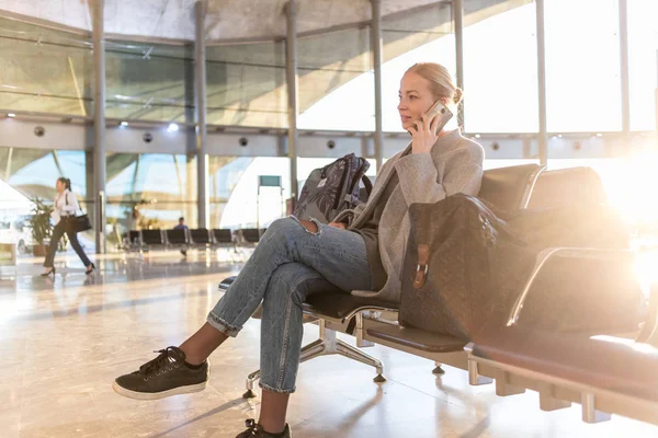 Kvinnliga resenären talar i hennes mobiltelefon medan du väntar på att ombord på ett plan på avgångsportarna på flygplats terminal. — Stockfoto