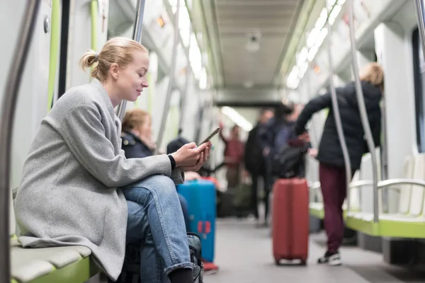 Vacker blond kvinna bär vinterpäls läsning på telefonen när du reser med tunnelbana kollektivtrafik. — Stockfoto