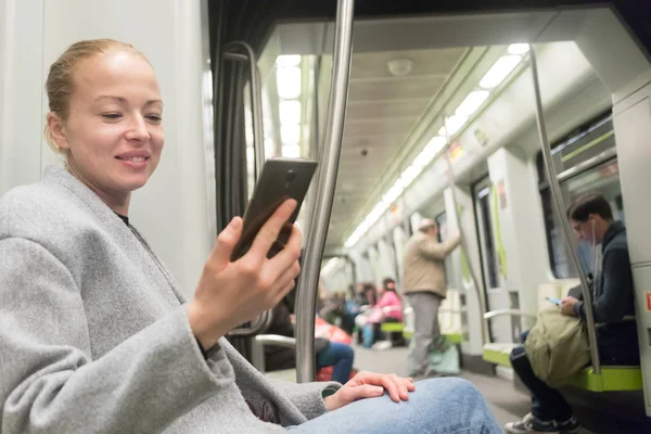 Schöne blonde Frau benutzt Smartphone während der Fahrt mit der U-Bahn. — Stockfoto