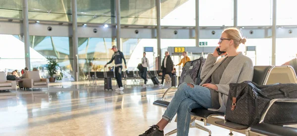 Mulher viajante conversando em seu telefone celular enquanto espera para embarcar em um avião nos portões de partida no terminal do aeroporto . — Fotografia de Stock