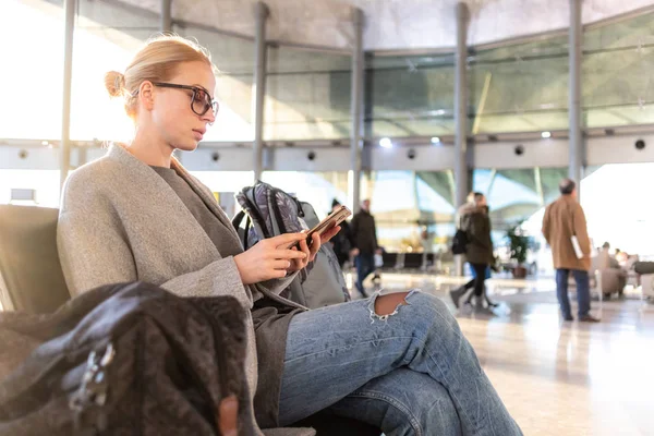 Viajero femenino usando su teléfono celular mientras espera para abordar un avión a las puertas de salida en la terminal del aeropuerto . —  Fotos de Stock