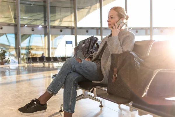 Viajera hablando en su teléfono celular mientras espera para abordar un avión a las puertas de salida en la terminal del aeropuerto . —  Fotos de Stock