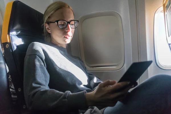 Жінка в окулярах читає на цифровому електронному пристрої читання під час подорожі літаком . — стокове фото