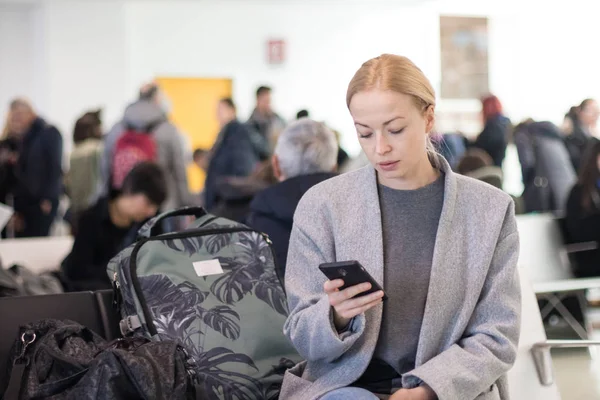 Mujer viajera leyendo en su teléfono celular mientras espera para abordar un avión a las puertas de salida en la terminal del aeropuerto . —  Fotos de Stock